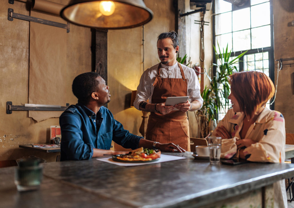 Restaurant server using handheld tablet for an ordering system with customers at table.